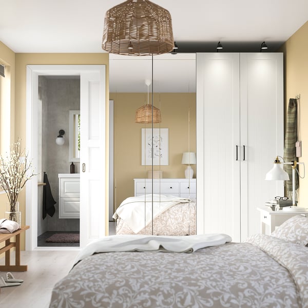 Minimalistische slaapkamer met grote gespiegelde PAX kledingkast, decoratieve verlichting en beige accenten.