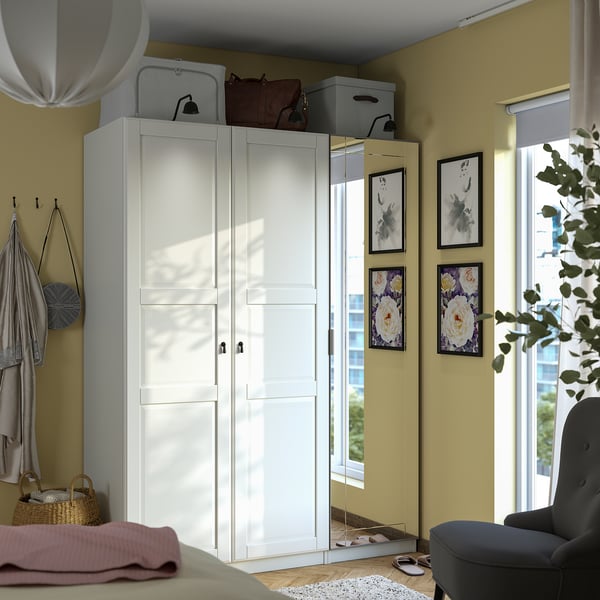 Goed georganiseerde kamer met witte PAX-kledingkast, spiegeldeuren, decoratieve items en natuurlijk licht.