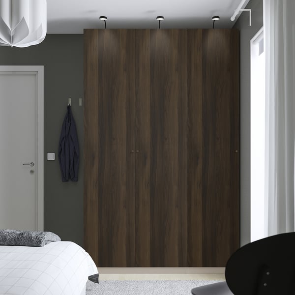 Moderne slaapkamer, grote houten PAX-kledingkast, donkere houten afwerking, overspanning van wandhoogte. Een wit bed en een grijze muur met haken zijn vlakbij.