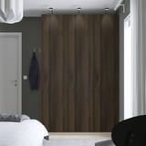 Moderne slaapkamer, grote houten PAX-kledingkast, donkere houten afwerking, overspanning van wandhoogte. Een wit bed en een grijze muur met haken zijn vlakbij.