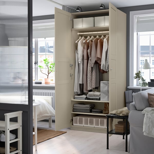 Open beige kledingkast met overhemden, opgevouwen kleding, onder planken, natuurlijk licht, grijze bank.