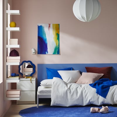 Moderne slaapkamer met PILTANDVINGE blauw dekbedovertrek. Witte planken met decoratieve artikelen, een kleurrijk schilderij en een stijlvolle hanglamp.