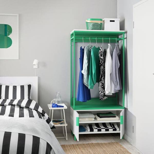 Een slaapkamer met een groene PLATSA kledingkast, opbergkleding en een gestreept bed.