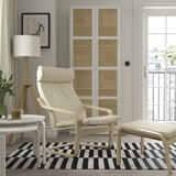 Moderne woonkamer met witte POÄNG-stoel, gestreept vloerkleed, lamp en plant.