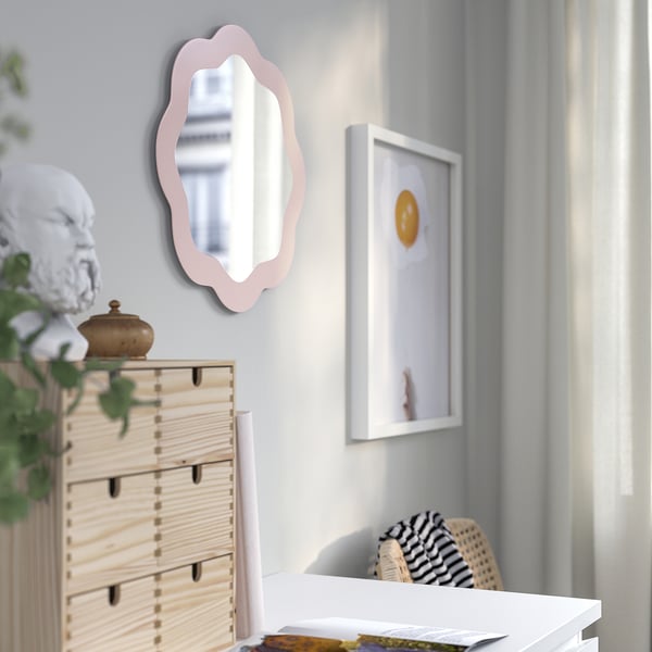 Blush ovale spiegel, gemonteerd aan de muur, reflecteert licht, versiert de kamer. Naast houten dressoir met witte buste decor.