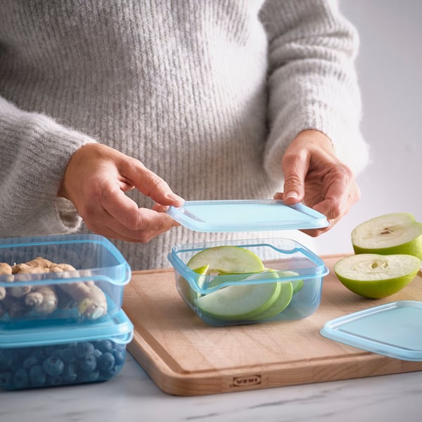 Persoon plaatst deksel op blauwe voedselcontainer met appelschijfjes, met praktische voedselopslag.