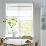 Moderne eethoek met RINGBLOMMA jaloezieën, ronde houten tafel, gevlochten stoel, citroen, glas en potplant.