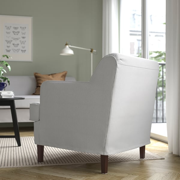 Gezellige woonkamer met gestreepte fauteuil, lamp, bank, boeken, schilderij en groot raam.