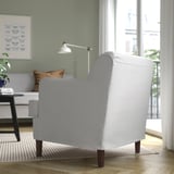 Gezellige woonkamer met gestreepte fauteuil, lamp, bank, boeken, schilderij en groot raam.