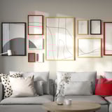 Moderne woonkamer met RÖDALM kaders in b/g/r/w, abstracte kunst. Grijze bank, houten salontafel met witte vaas en beker.