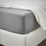 Netjes opgemaakte lakens met een glad, grijs bovenlaken en witte kussenslopen op een matras. Het hoeslaken met elastische randen houdt het stevig op zijn plaats.