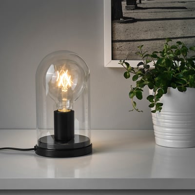 Heldere glazen lamp en plant op tafel, foto achter.