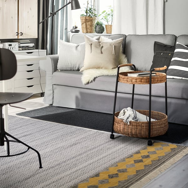 Moderne woonkamer met grijs RYSSGRÄS vloerkleed, comfortabele sectionele en gevlochten mandenwagen.