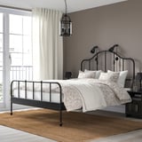 Gezellige slaapkamer met donker metalen SAGSTUA bed, messing details, keurig beddengoed, hanglamp, groot raam, nachtkastje, vloerkleed.