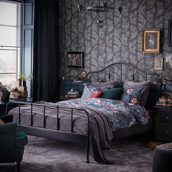 Donkere slaapkamer: kleurrijk bed, groene stoel, groot raam, decor.