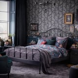 Donkere slaapkamer: kleurrijk bed, groene stoel, groot raam, decor.