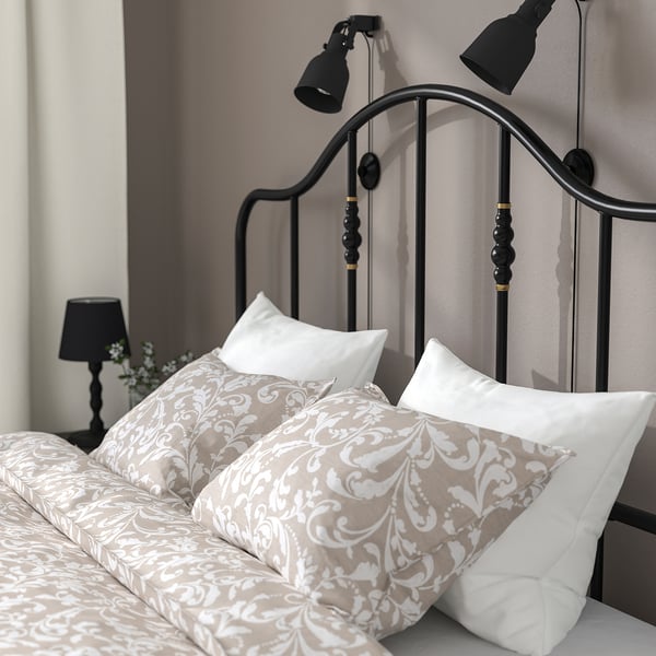 Een stijlvol zwart metalen bedframe met messing accenten, voorzien van een gebogen hoofdeinde en verstelbare leeslampjes aan de muur.