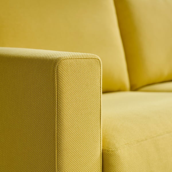 Close-up van een geel gestoffeerde bank met armleuning, met zachte, getextureerde stof en schone stiksels.