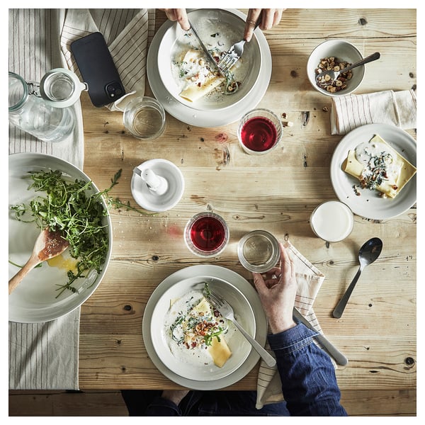 Een houten tafel met rustieke, aardse grijze steengoed borden, schalen en glazen. Mensen genieten van eten en drinken in een gezellige, informele eetomgeving.