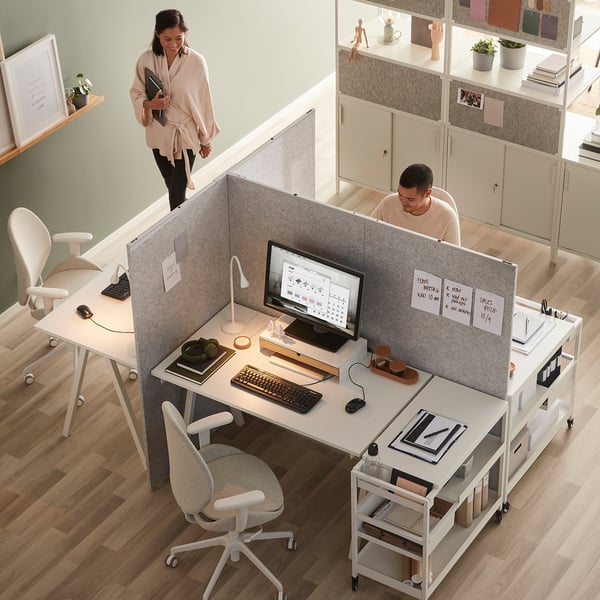 Modern kantoor met SIDORNA-verdelers; één staand met tablet, één aan bureau met computer; Versierd met planken en planten.