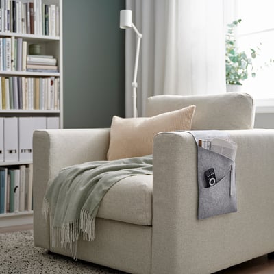 Moderne woonkamer met grijze SILÄNG stoel, plei, crèmekleurig kussen, opslag met camera, pen, tijdschrift. Witte boekenkast op de achtergrond.