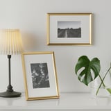 Gouden fotolijsten met zwart-witfoto's en een vlinder, geplaatst op een tafel met een lamp en een plant.
