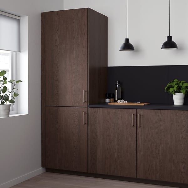 Moderne keuken met hoge donkerhouten SINARP kasten, strakke handgrepen en zwart aanrechtblad. Twee hanglampen boven, planten naast het raam.
