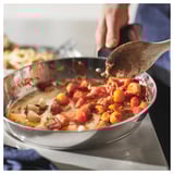 Een chef-kok roert tijdens het koken in een pan met tomaten en knoflook.