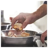 Persoon die knoflook in de SLÄTROCKA zilveren pan plaatst en zich voorbereidt om te koken.