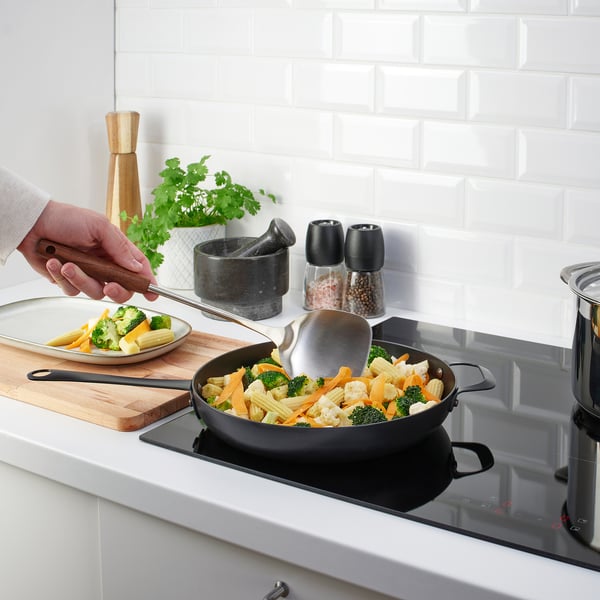 De persoon kookt groenten met een roestvrij staalspatel. Het keukengerei heeft een stevige handgreep, ideaal om mee te koken.