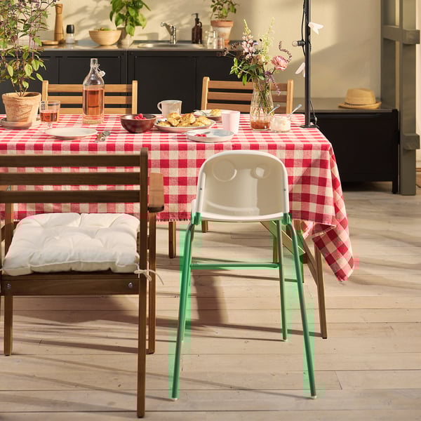 Zonnige keuken met roodgeruite tafelsetting, witte kinderstoel en potplanten.