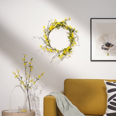 Gele bank, bloemenkrans, vaas met bloemen op tafel, witte bloemenkunst.