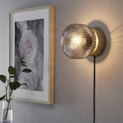 Moderne wandlamp in glanzend messing met grijze glazen kap, die zacht sfeerlicht werpt.