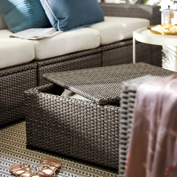 Gezellige terrasscène met SOLLERÖN grijze rotan rieten sectional, pluche witte kussens, blauwe kussens en een salontafel.