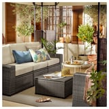 Buitenlounge met SOLLERÖN grijze rieten bank, kleurrijke kussens, salontafel, sandalen en planten.