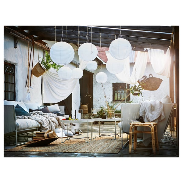 Buitenterras met witte hangende SOLVINDEN lampen, comfortabele stoelen, vloerkleed, planten en dekens.