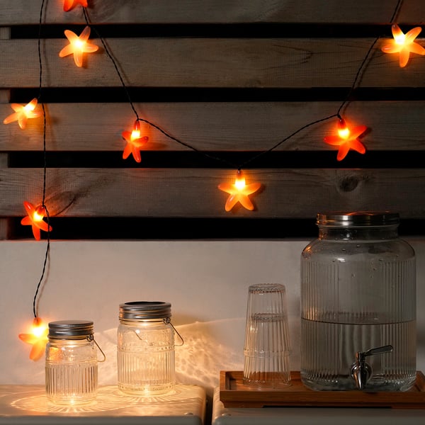 Oranje sterlichten boven potten op houten plank, waardoor een warme gloed ontstaat.