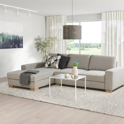 Moderne woonkamer met grijze bank, kussens, salontafel, plant, vloerkleed en grote ramen.