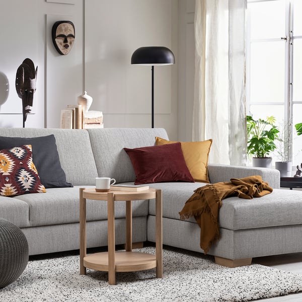 Moderne woonkamer met een lichtgrijze SÖRVALLEN-bank, kleurrijke kussens, houten bijzettafel, zwarte vloerlamp en groot raam.