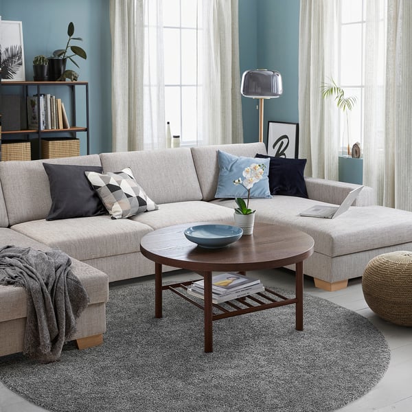Moderne woonkamer met grijze SÖRVALLEN-bank, houten salontafel, blauwe accenten en grote ramen met witte gordijnen.