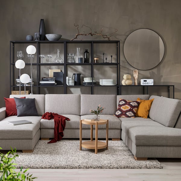 Moderne woonkamer met grijze SÖRVALLEN sectionals, kleurrijke kussens, houten salontafel en zwarte rek met decoratieve items.