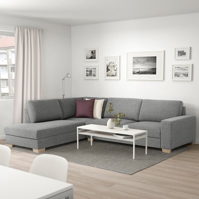 Moderne grijze SÖRVALLEN sectionele bank met kussens, salontafel, tegen groot raam, lichte inrichting, minimalistische kunst.