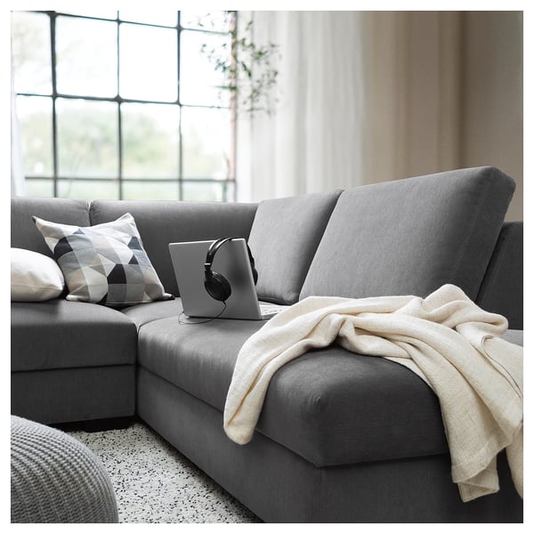 Moderne grijze stoffen bank met kussens en deken, digitale tablet en koptelefoon.