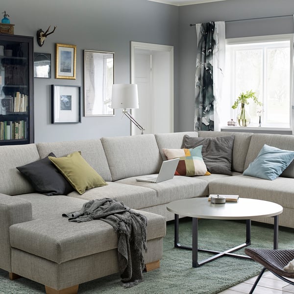 Moderne grijze l-vormige bank met kleurrijke kussens, een knusse deken en een strakke salontafel in een stijlvolle woonkamer.