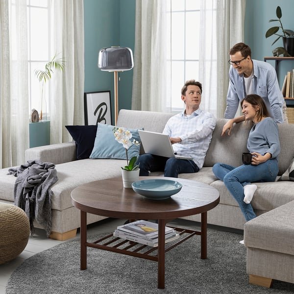 Moderne woonkamer met een lichtgrijze SÖRVALLEN-bank, houten salontafel en mensen die laptops en een mok gebruiken.