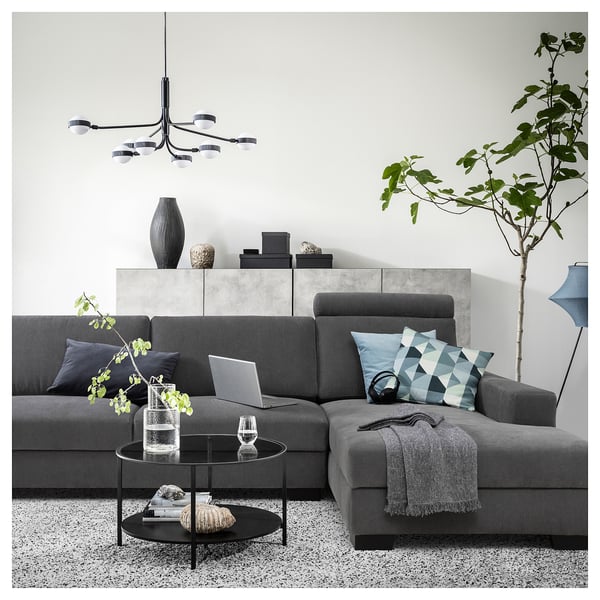 Moderne woonkamer met grijze SÖRVALLEN-bank, glazen salontafel, kussens met patroon, hanglamp en potplant.