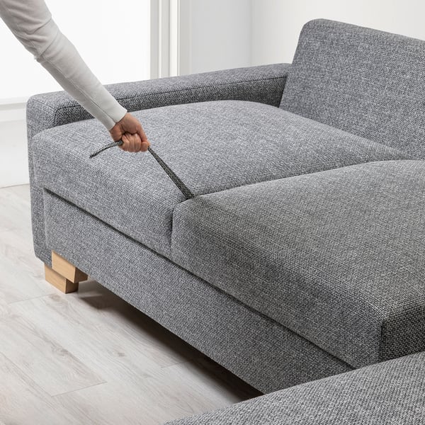 Persoon opent slaapbanken opbergvak. Moderne grijze bank kan worden omgebouwd tot bed, houten poten.