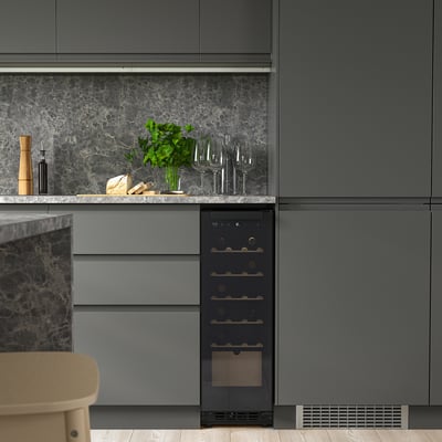 Moderne keuken met strakke zwarte wijnkoeler tussen grijze kasten, met wijnflessen en glazen, in contrast met marmeren achterwand.
