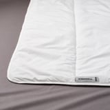 Wit beddekbed met subtiele stiksels, grijs label, netjes op bed.