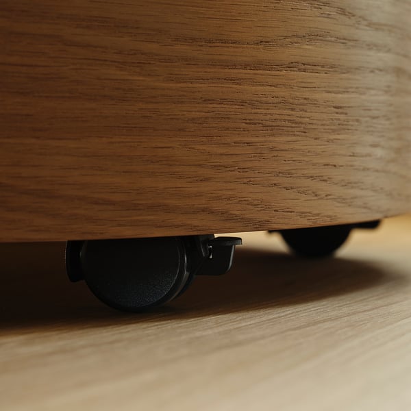 Close-up van de onderkant van een licht houten meubel, met een verborgen zwenkwiel voor gemakkelijke verplaatsing.
